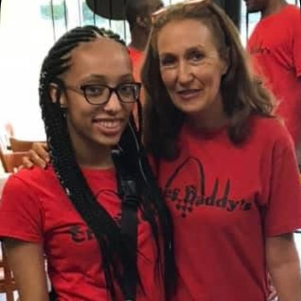 Two smiling women in red Chef Daddy's t-shirts, one with glasses and braids, the other with long brown hair.
