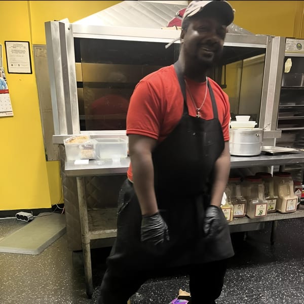 Chef Daddy's chef, wearing a red shirt and black apron, smiles in a southern kitchen.