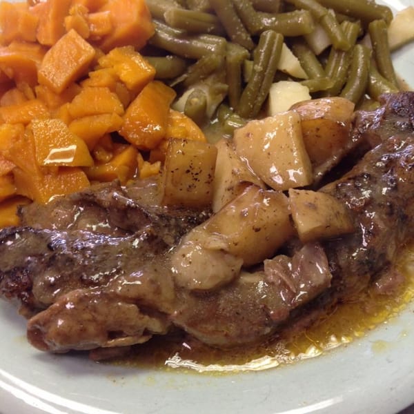 A southern meal with smothered steak, potatoes, green beans, and candied yams on a white plate.