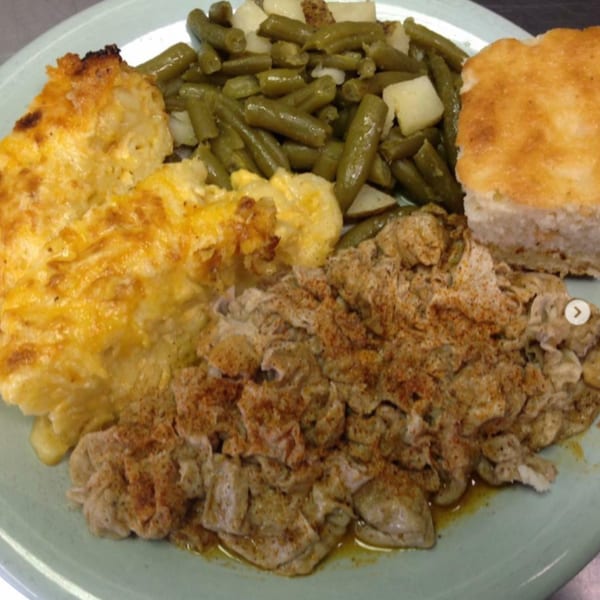A southern meal with macaroni and cheese, green beans, chicken, and cornbread on a light blue plate.